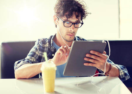 Leisure, technology, communication and people concept - Creative man with tablet pc computer and earphones listening to music at cafe tableの写真素材