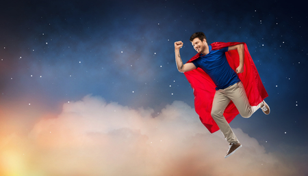 Super power and people concept - Happy young man in red superhero cape flying in air over starry night sky backgroundの写真素材