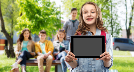 Education, school and people concept - happy smiling teenage student girl with bag showing blank tablet computer screen over group of friends outdoors backgroundの写真素材