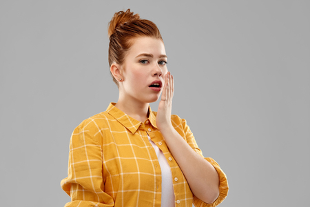 emotion, expression and people concept - red haired teenage girl in checkered shirt covering mouth by hands over grey backgroundの写真素材