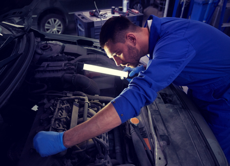 Mechanic man with lamp repairing car at workshop