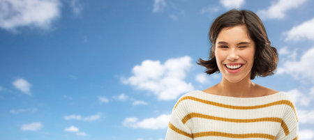 Happy smiling woman winking over blue skyの写真素材