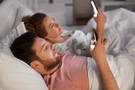 couple using smartphones in bed at nightの写真素材
