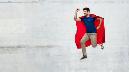 man in red superhero cape jumping over concreteの写真素材