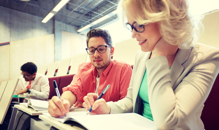education, high school, university, learning and people concept - group of international students with notebooks writing at lecture hallの写真素材
