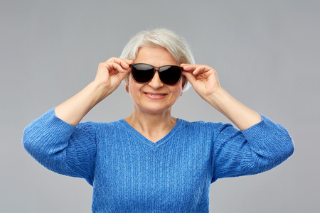 Valentine's day, summer and old people concept - portrait of smiling senior woman in red black sunglasses over grey backgroundの写真素材