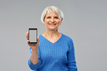 Technology and old people concept - smiling senior woman showing smartphone over grey background