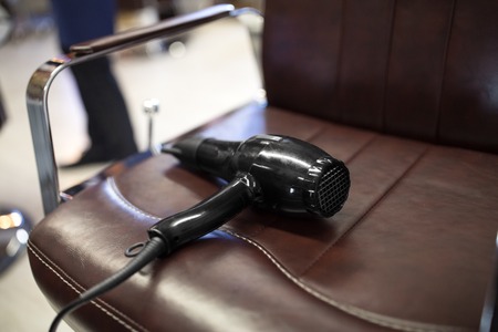 tools, grooming and hairdressing concept - black hair dryer on brown leather chair seat at barbershopの写真素材