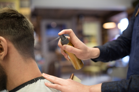 grooming, hairdressing and people concept - hairstylist applying styling spray to male client's hair at barbershopの写真素材