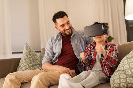 family, virtual reality and entertainment concept - happy father and little son in vr glasses playing video game at homeの写真素材
