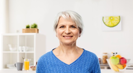 old people concept - portrait of smiling senior woman in blue sweater over kitchen background