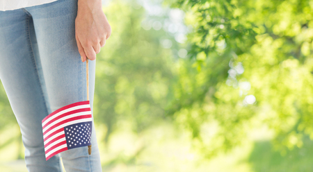 independence day, celebration, patriotism and holidays concept - close up of woman legs and hand holding american flag at 4th july over green natural backgroundの写真素材