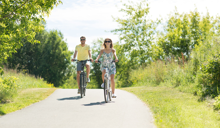 people, leisure and lifestyle concept - happy young couple riding bicycles along road in summerの写真素材