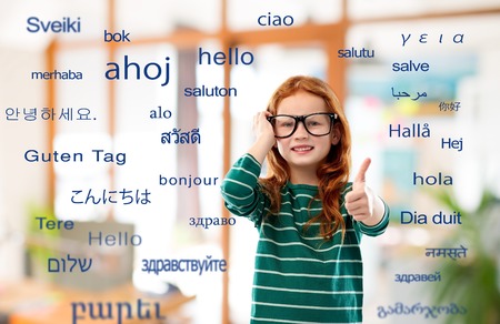 education, translation and learning concept - smiling red haired student girl in glasses and green striped shirt over greeting words in different foreign languages on backgroundの写真素材