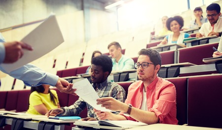 education, high school, university, learning and people concept - teacher giving tests to students at lectureの写真素材