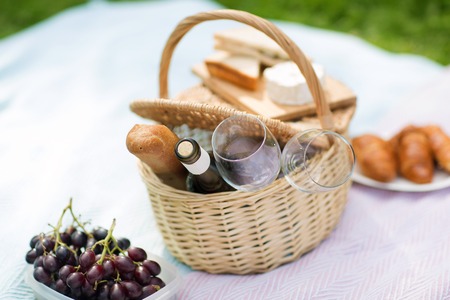 leisure concept - picnic basket, food and wine glasses on blanket at summer parkの写真素材