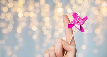 childhood and body part concept - close up of hand holding pinwheel toy over festive lights backgroundの写真素材