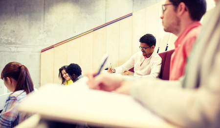 education, high school, university, learning and people concept - group of international students with notebooks writing in lecture hallの写真素材