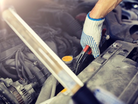 car service, repair, maintenance and people concept - auto mechanic man with lamp and pliers working at workshopの写真素材