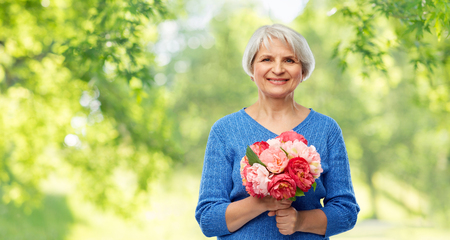 holidays, old age and people concept - happy smiling senior woman with flowers over green natural backgroundの写真素材