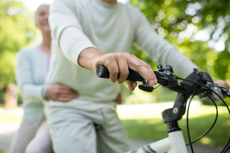 active old age, people and lifestyle concept - happy senior couple riding one bicycle together at summer parkの写真素材