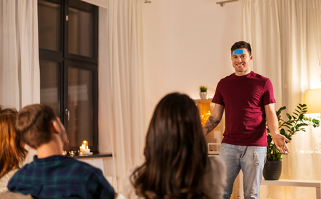 friendship, leisure and entertainment concept - happy friends playing guessing game at home in eveningの写真素材