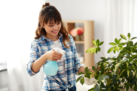 happy asian woman spraying houseplant at homeの写真素材
