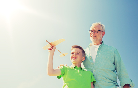 senior man and boy with toy airplane over skyの写真素材
