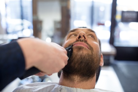 man and barber with trimmer cutting beard at salonの写真素材