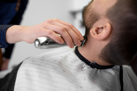 man and barber with trimmer cutting beard at salonの写真素材