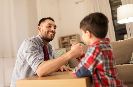 happy father and little son arm wrestling at homeの写真素材