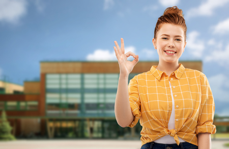 red haired teenage girl showing ok over schoolの写真素材