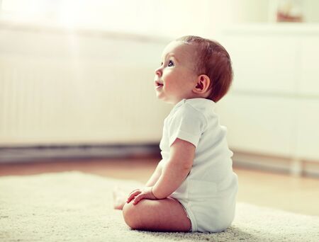 happy baby boy or girl sitting on floor at homeの写真素材