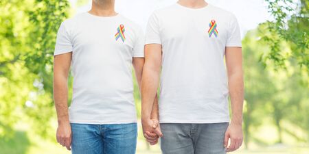 lgbt, same-sex relationships and homosexual concept - close up of male couple with gay pride rainbow awareness ribbons over green natural backgroundの写真素材