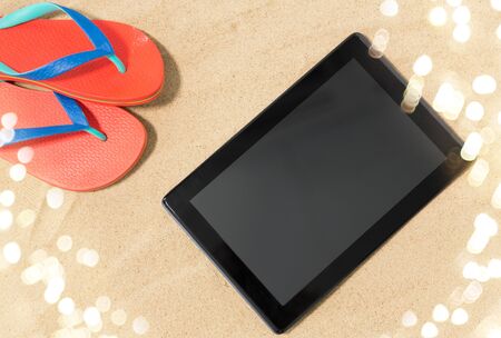 technology, vacation and summer holidays concept - tablet computer and flip flops on beach sandの写真素材