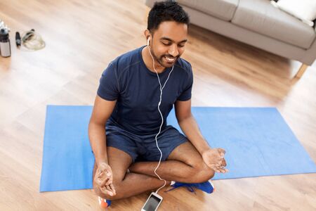 indian man meditating in lotus pose at homeの写真素材
