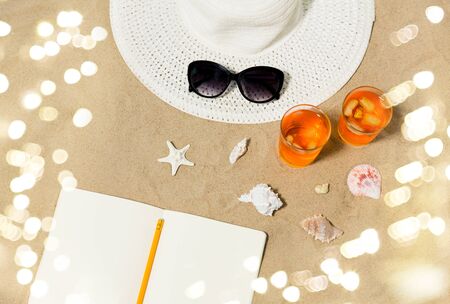 Notebook, cocktails, hat and shades on beach sand