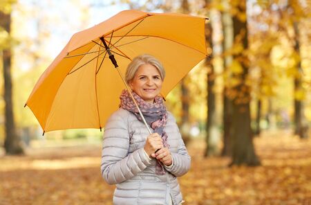 old age, weather and season concept - portrait of happy senior woman with umbrella at autumn parkの写真素材