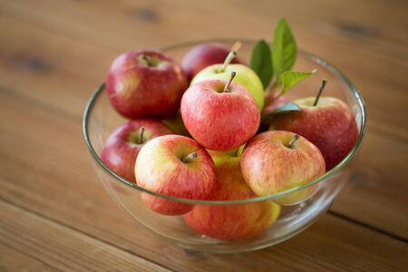 fruits, food and harvest concept - ripe apples in glass bowl on wooden tableの写真素材