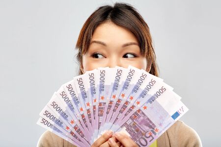 people, ethnicity and portrait concept - happy asian young woman holding hundreds of euro money...