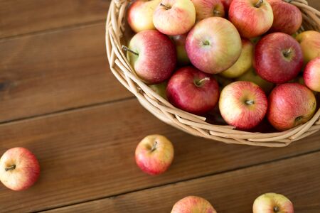 Fruits, food and harvest concept - ripe apples in wicker basket on wooden tableの写真素材