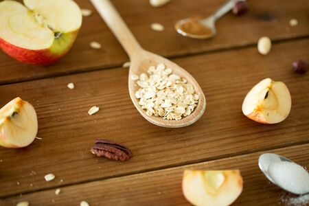 Oatmeal in wooden spoon, cut apples and nutsの写真素材