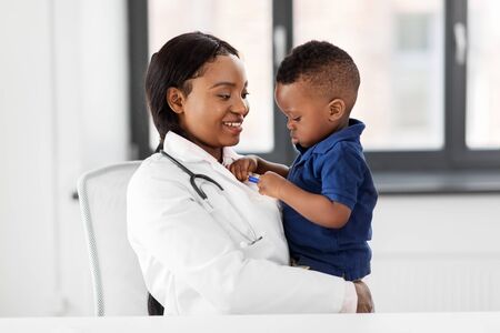 Medicine, healthcare, pediatric and people concept - happy African American female doctor or pediatrician holding baby boy patient on medical exam at clinicの写真素材