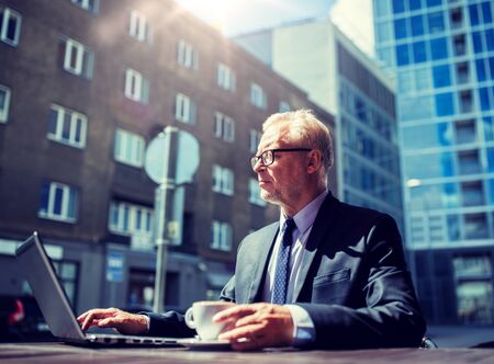 Business, technology and people concept - senior businessman with laptop computer drinking coffee at city street cafeの写真素材