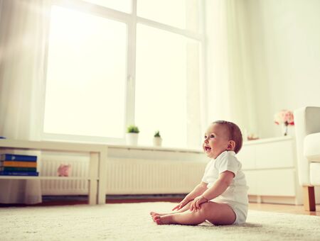 Happy baby boy or girl sitting on floor at homeの写真素材