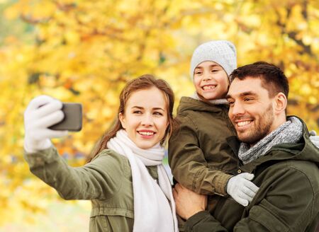 family taking selfie by smartphone in autumn parkの写真素材