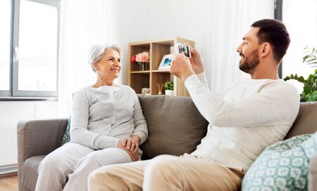 adult son photographing senior mother at home