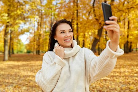Woman taking selfie by smartphone at autumn park