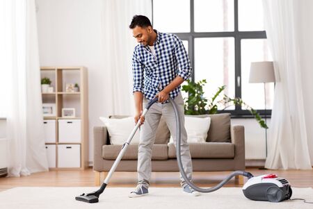 Household and cleaning concept - Indian man with vacuum cleaner at homeの写真素材