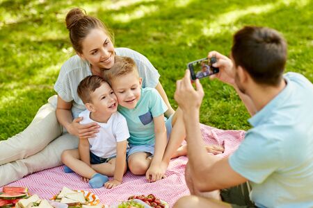 Father taking picture of family on picnic at parkの写真素材